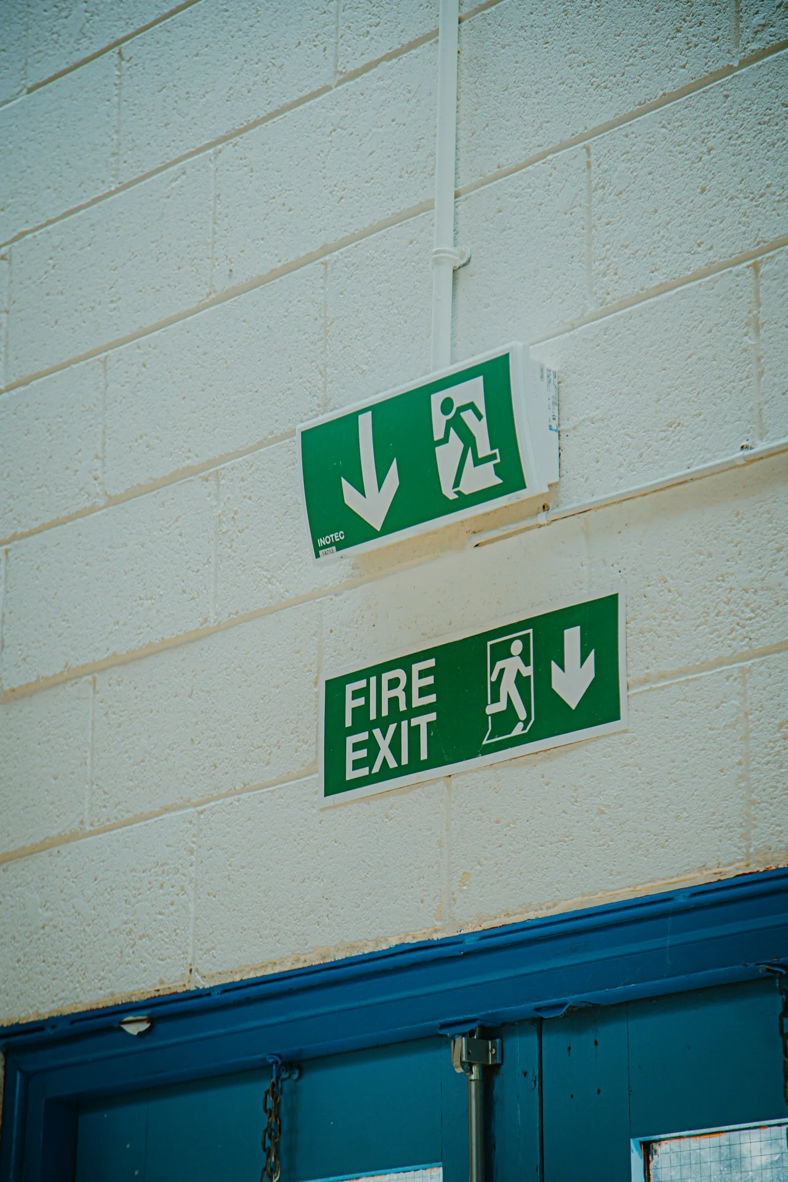 Green fire exit signs with running-man pictograms above a blue fire door
