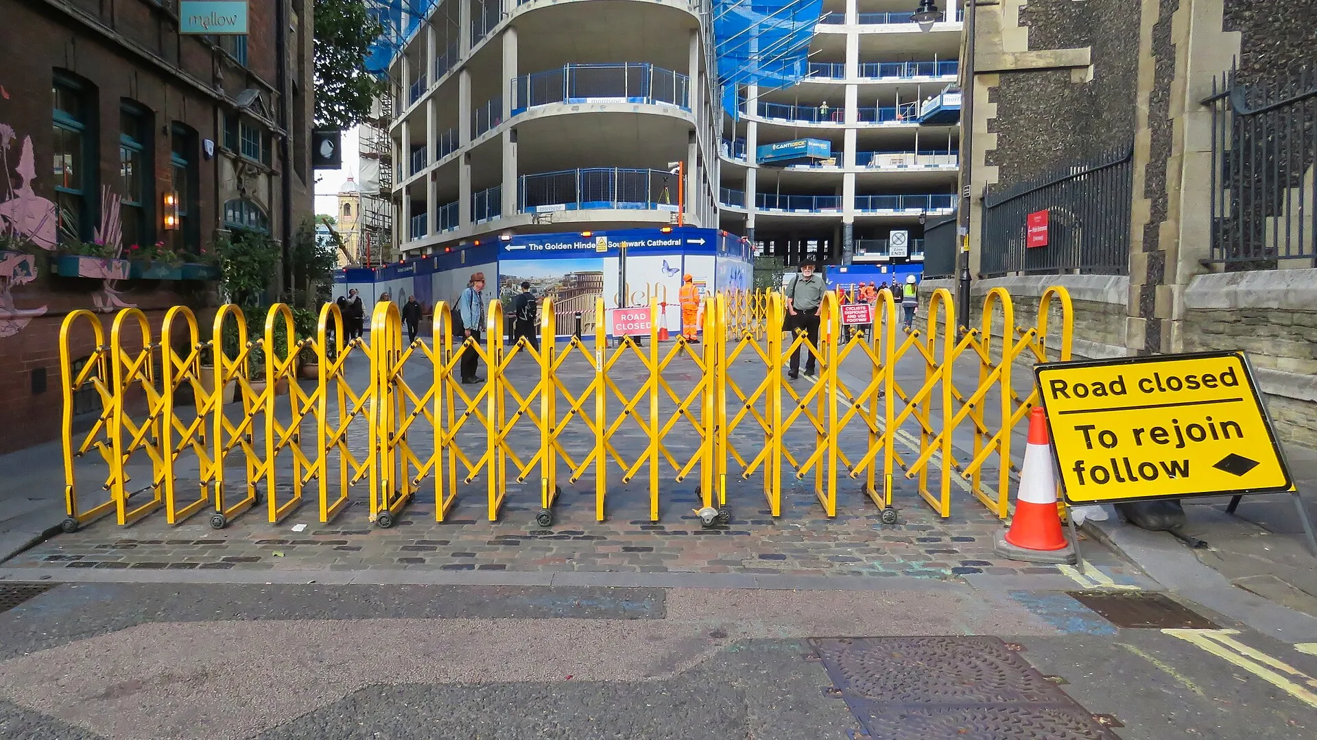 Yellow expanding steel barrier across a road with Road closed sign and traffic cone