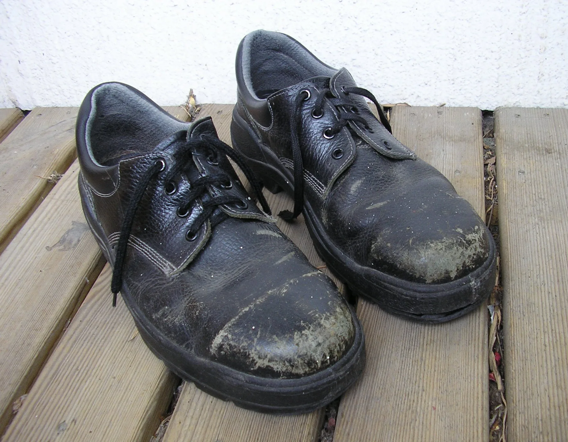 Pair of well-worn black leather steel-toe safety shoes on decking