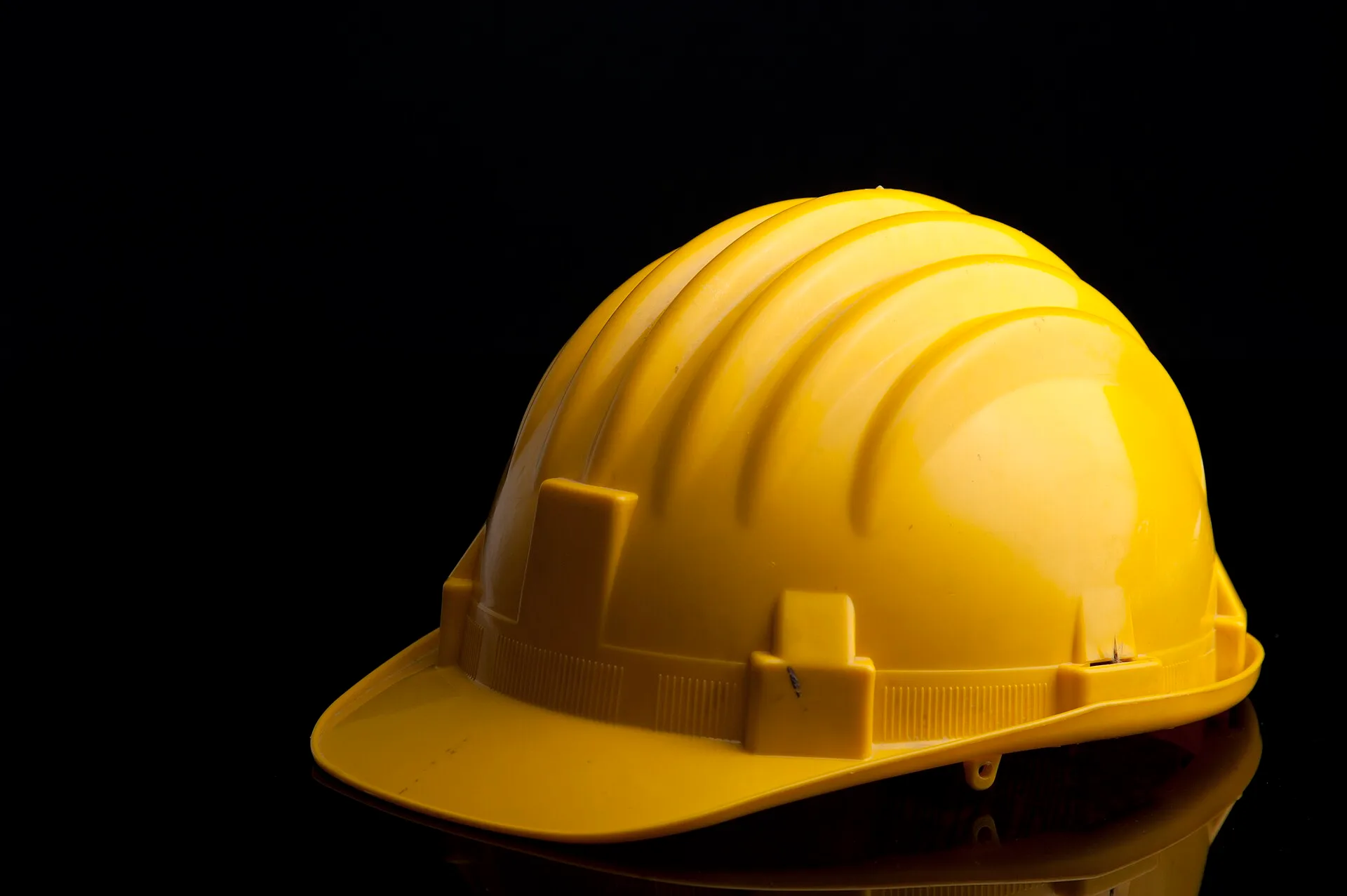 Yellow hard hat with ribbed shell on a black studio background