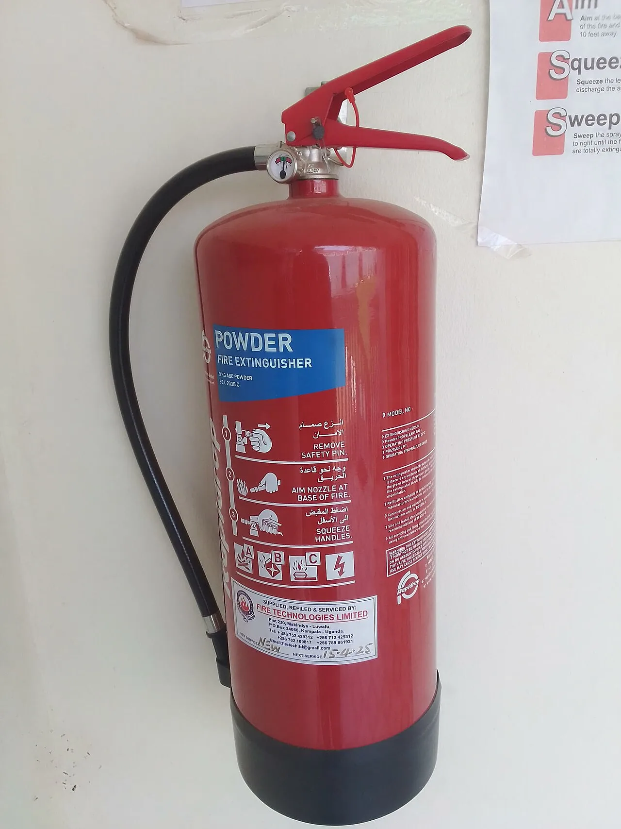Red stored-pressure dry powder fire extinguisher with black hose mounted on a white wall