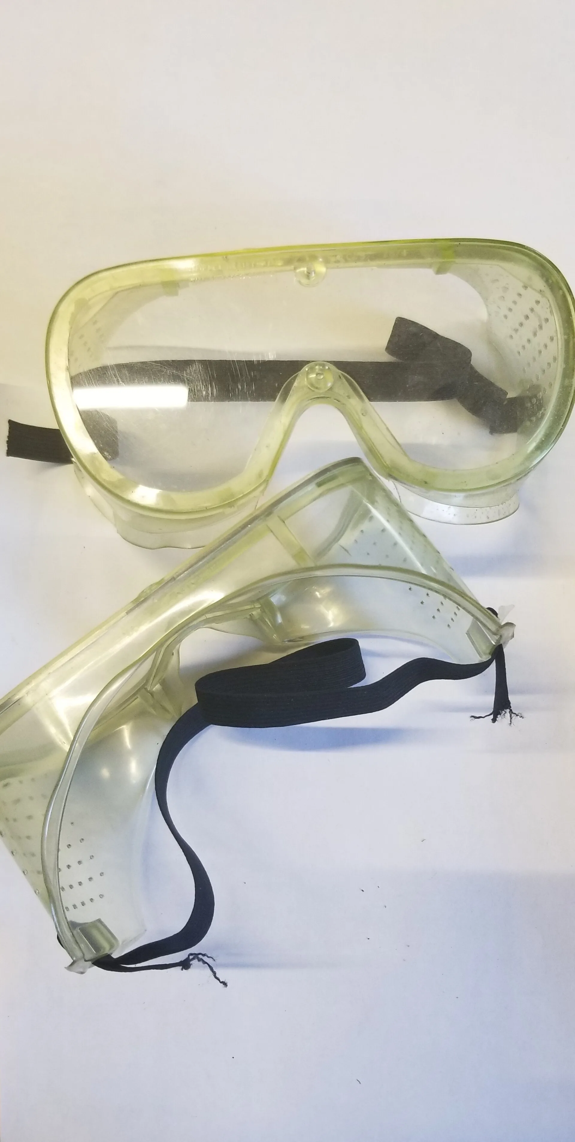Two clear vented safety goggles with elastic straps on a white background