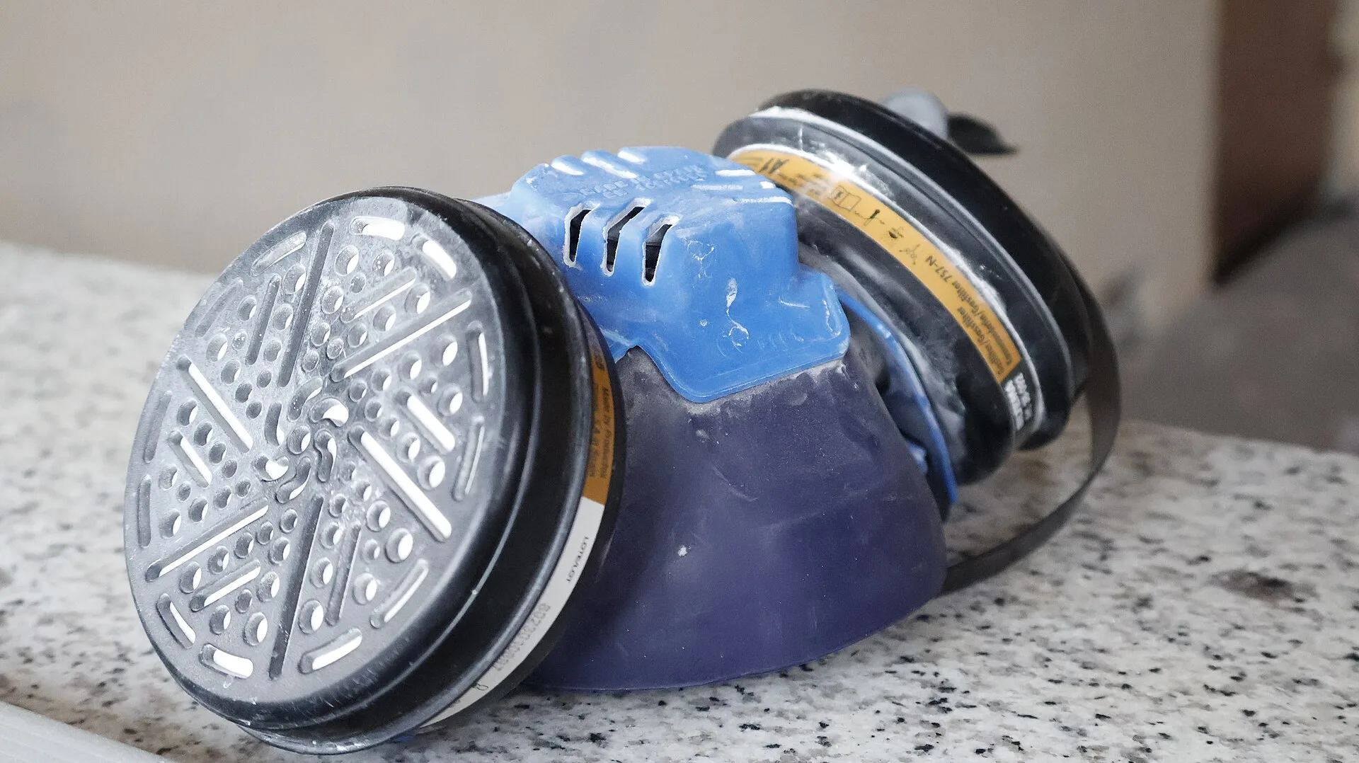Blue reusable half-mask respirator with twin round filters on a granite surface