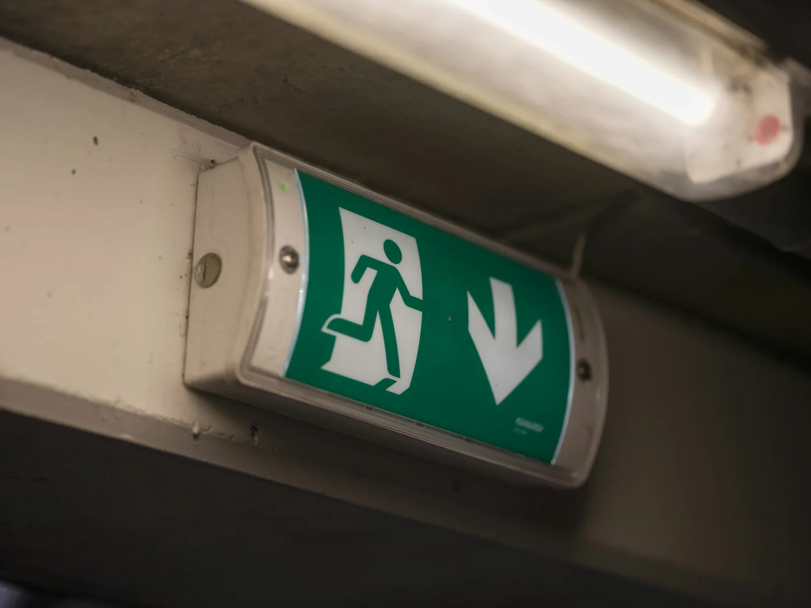 Wall-mounted emergency exit luminaire with running-man and down-arrow legend
