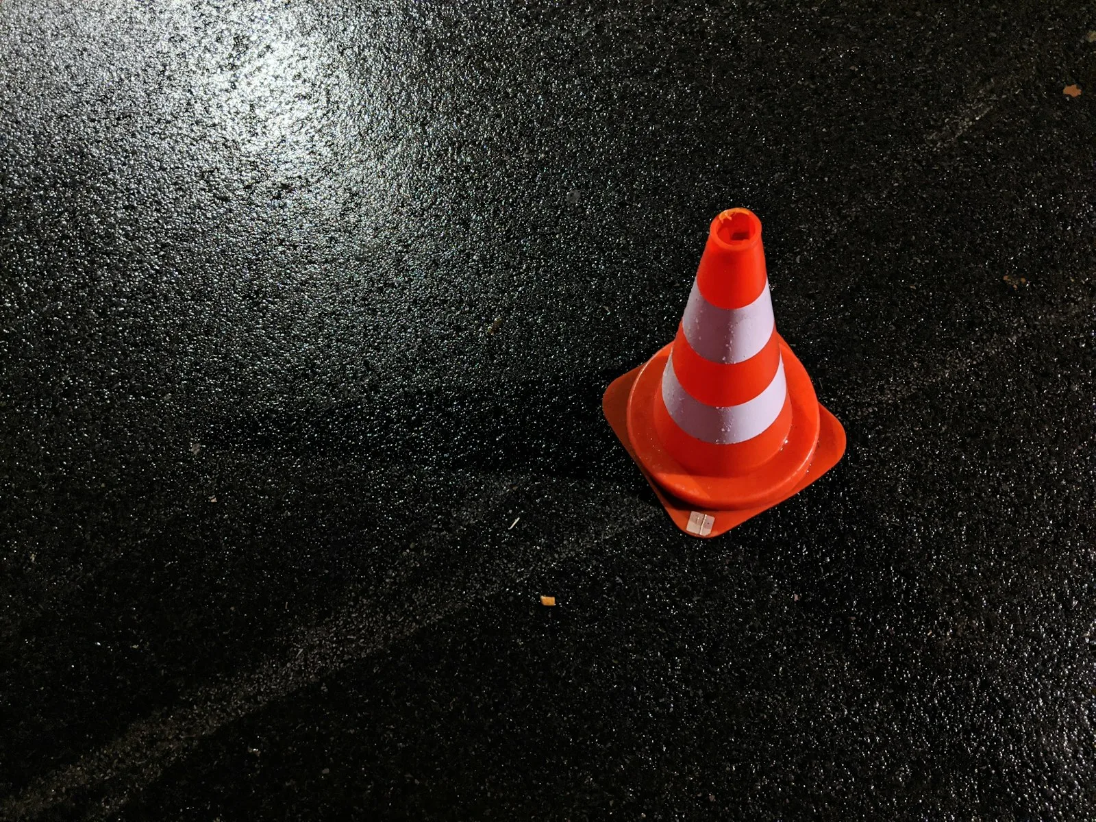 Orange traffic cone with white reflective bands on dark wet asphalt