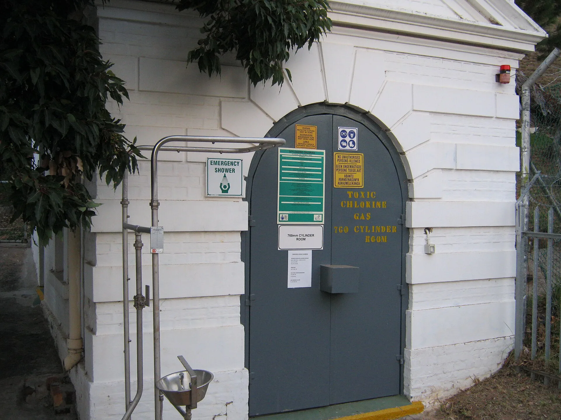 Emergency safety shower and stainless eyewash fountain beside a chlorine cylinder store door