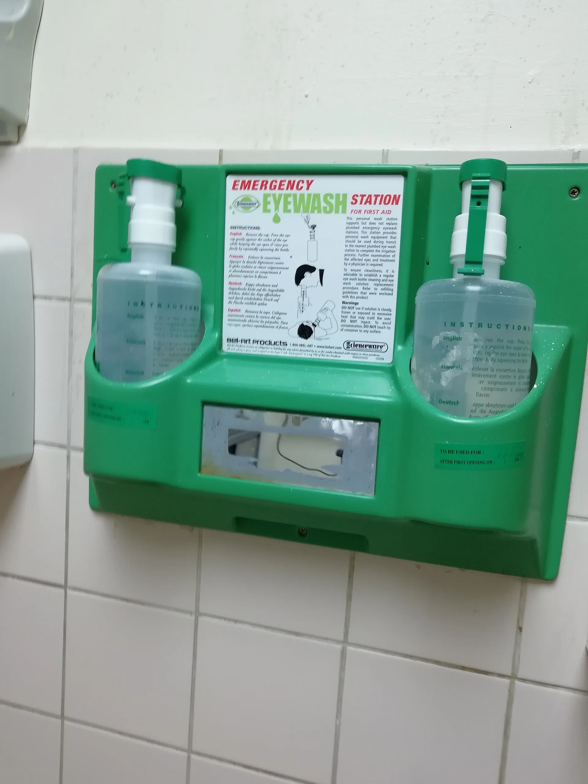 Green wall-mounted emergency eyewash station holding two eyewash bottles