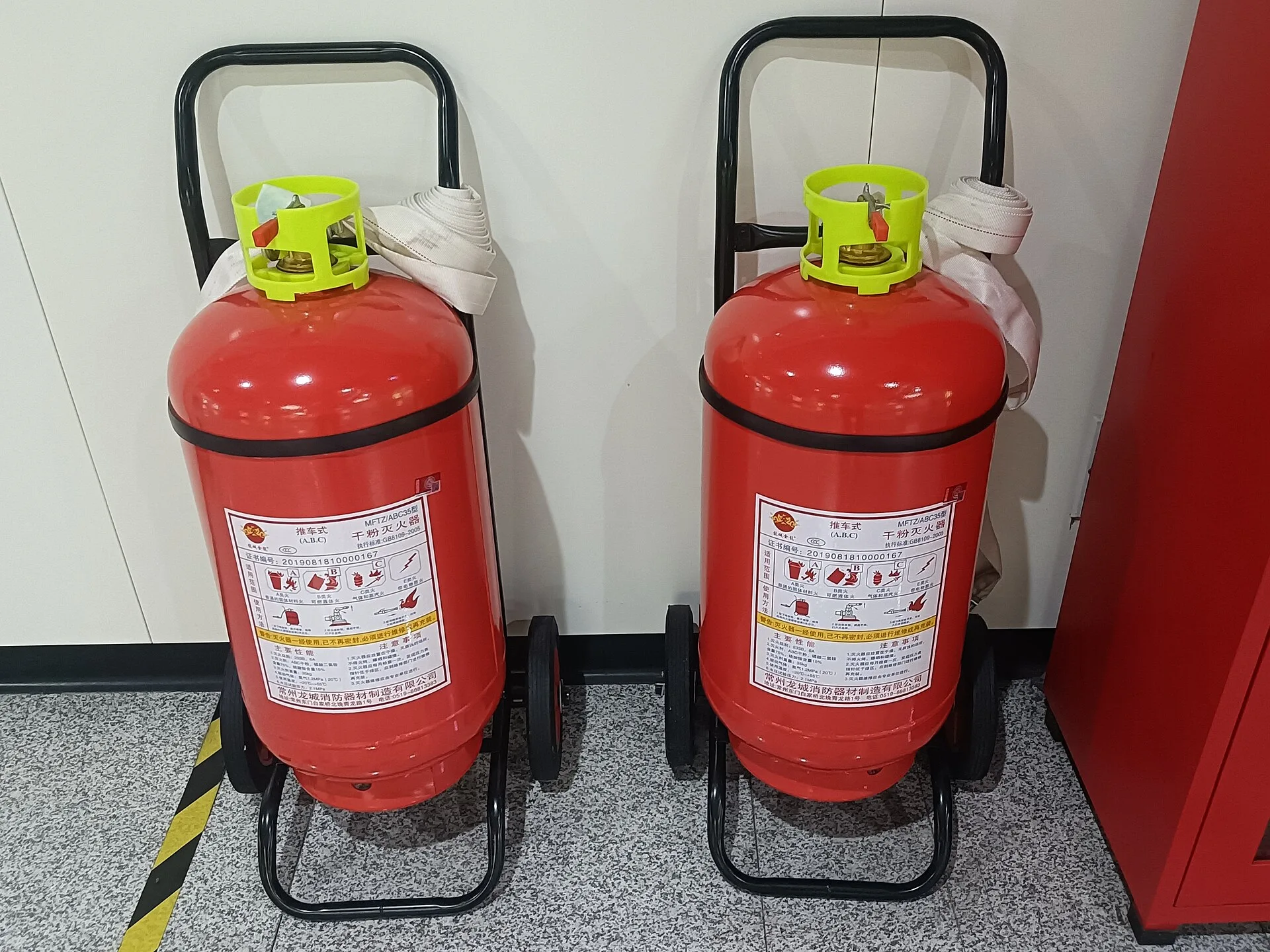 Two large red wheeled fire extinguishers on trolleys with rolled hoses