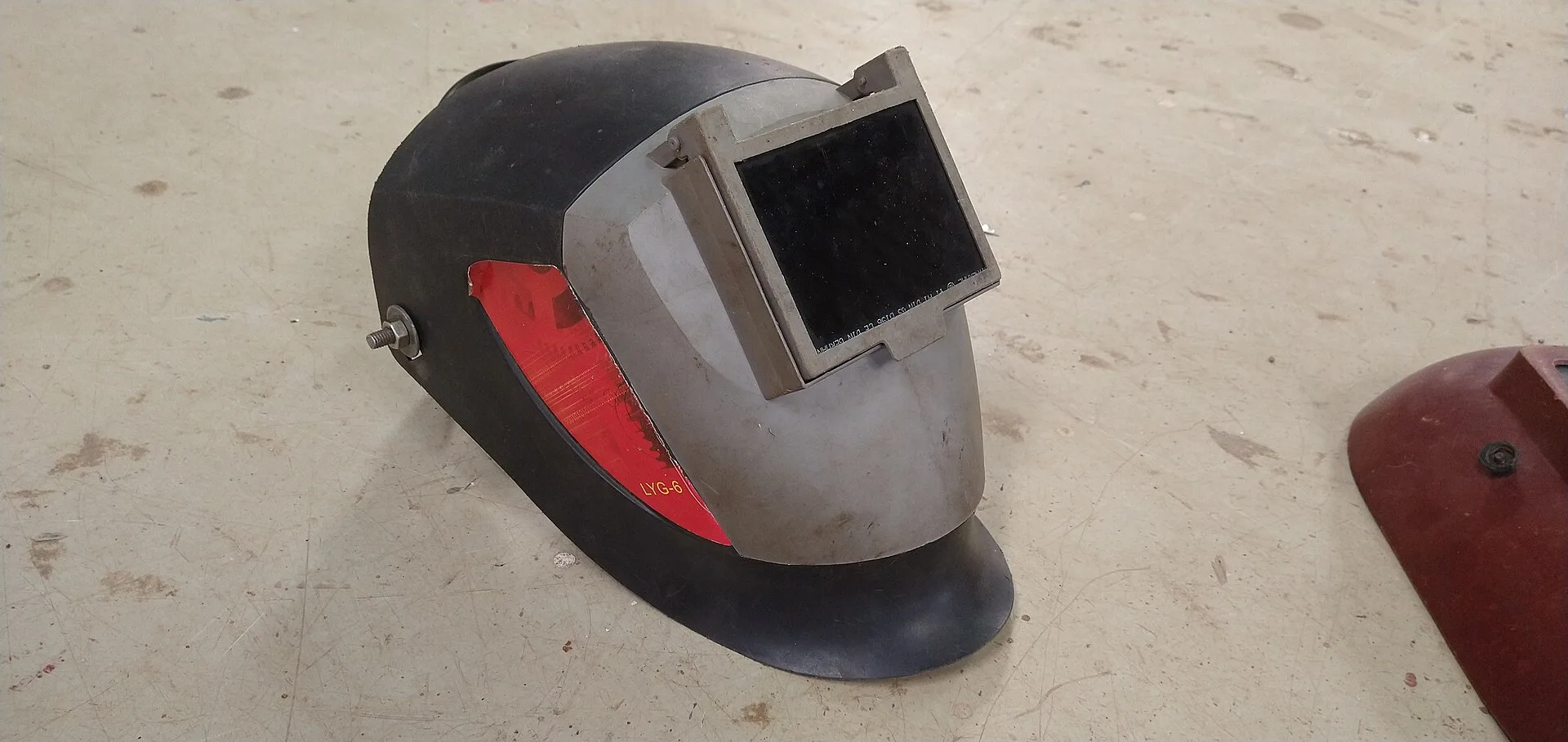 Grey welding helmet with flip-up filter window lying on a workshop floor