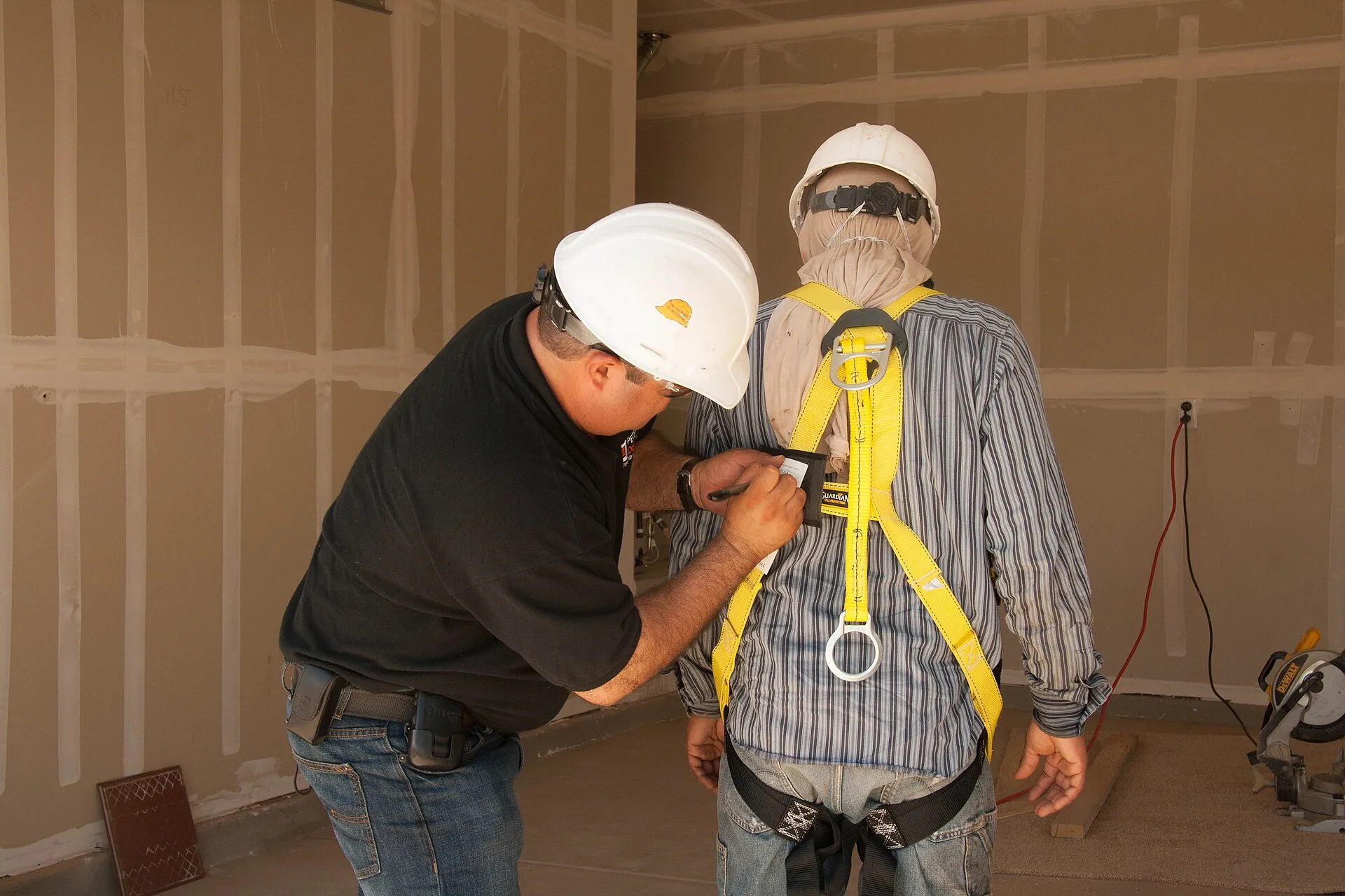 Instructor adjusting a yellow full-body fall-arrest harness on a worker