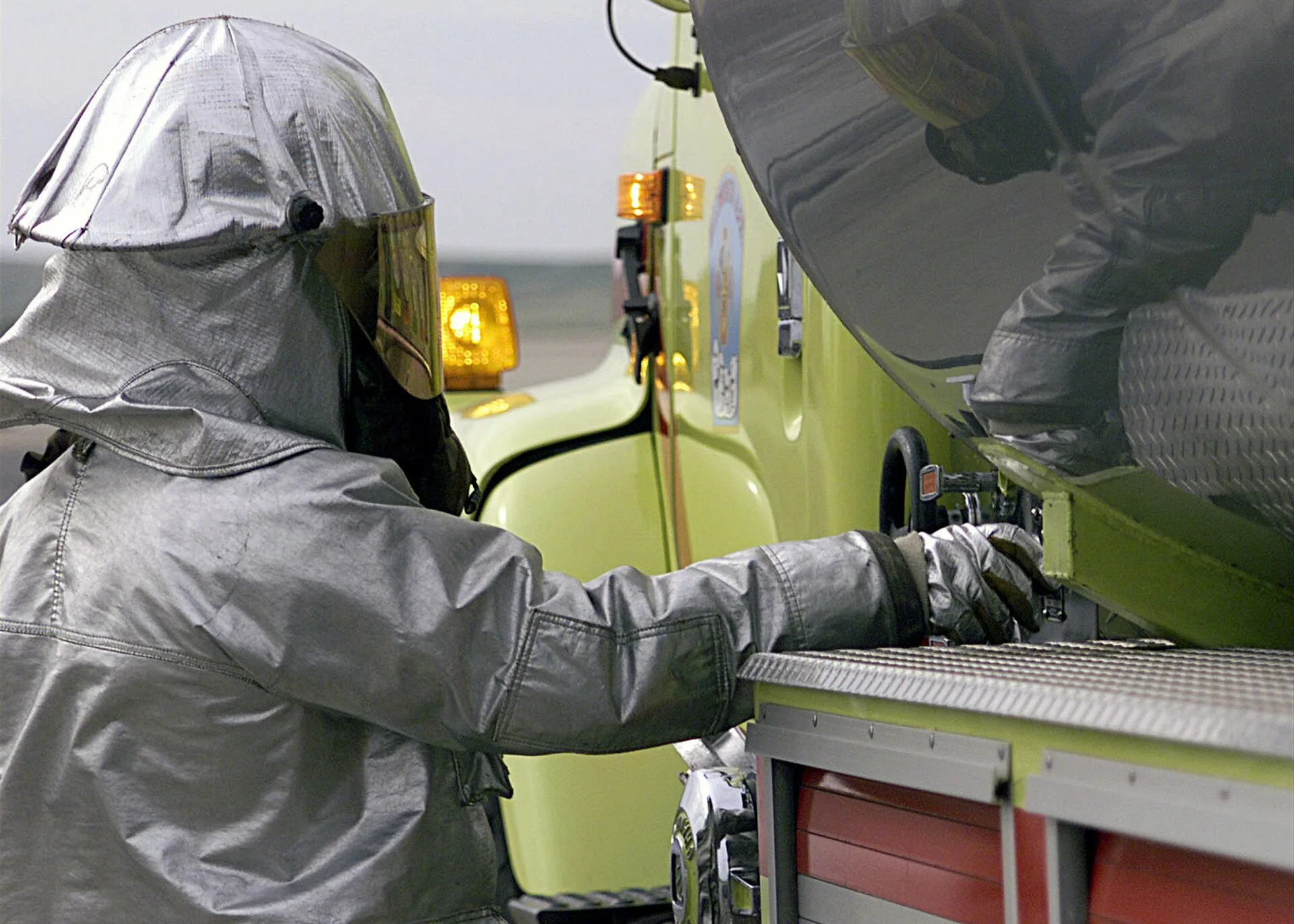Firefighter in an aluminised close-proximity suit and hood operating a fire truck