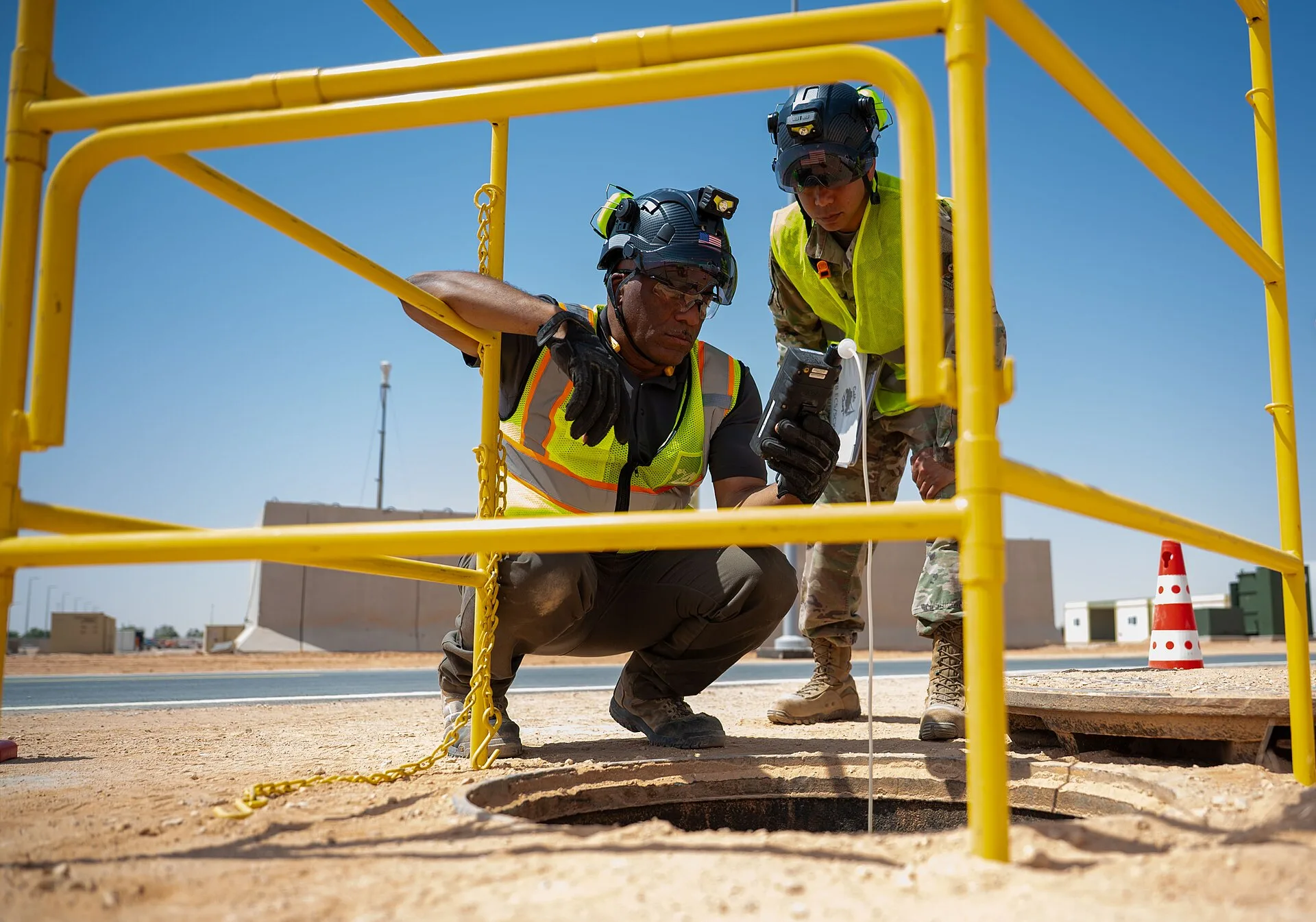 Workers in hi-vis vests using a portable gas detector to test the atmosphere of a manhole before confined-space entry
