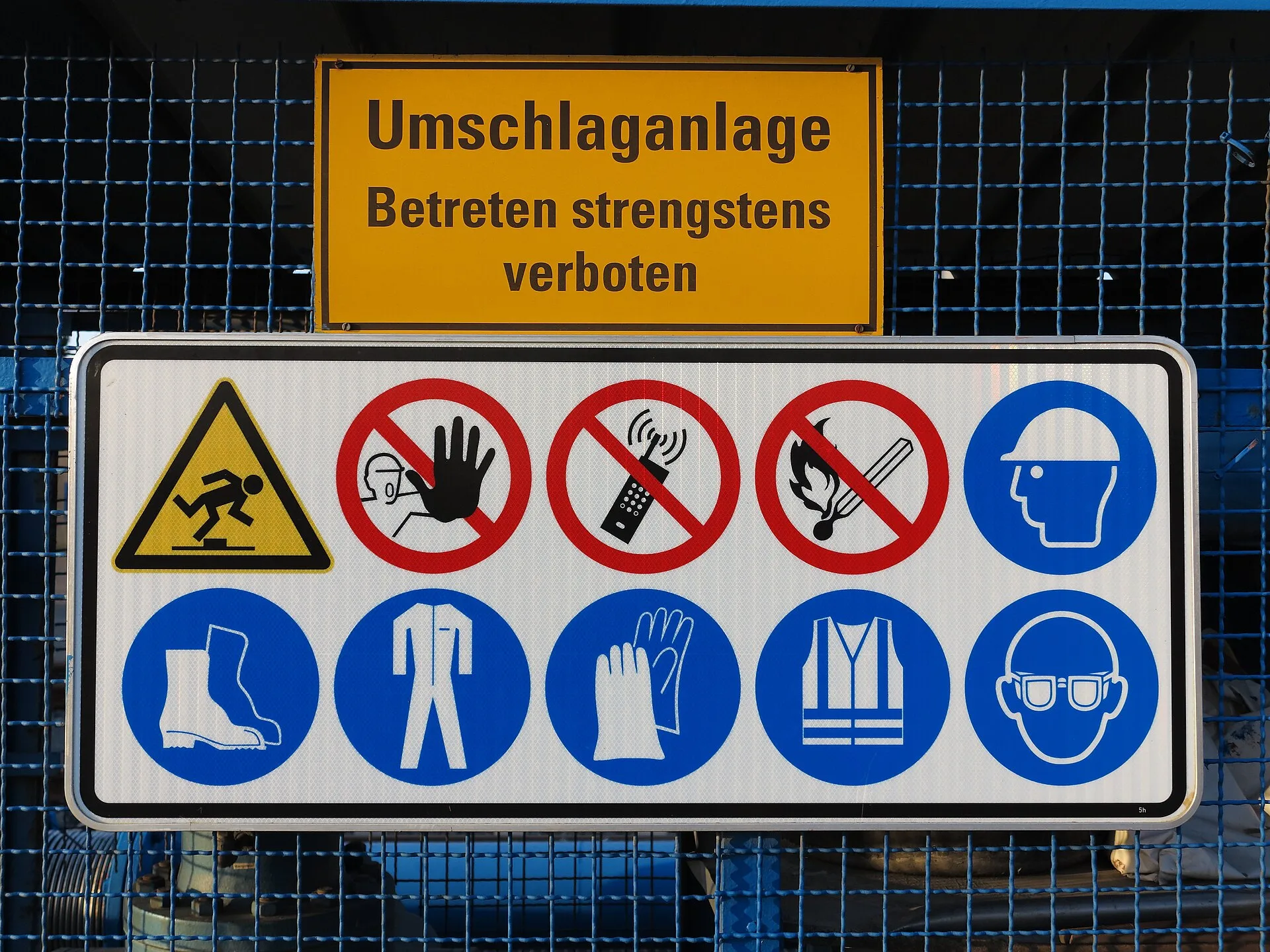 Site safety sign board combining warning, prohibition and blue mandatory PPE pictograms for hard hat, boots, overalls, gloves, hi-vis and goggles