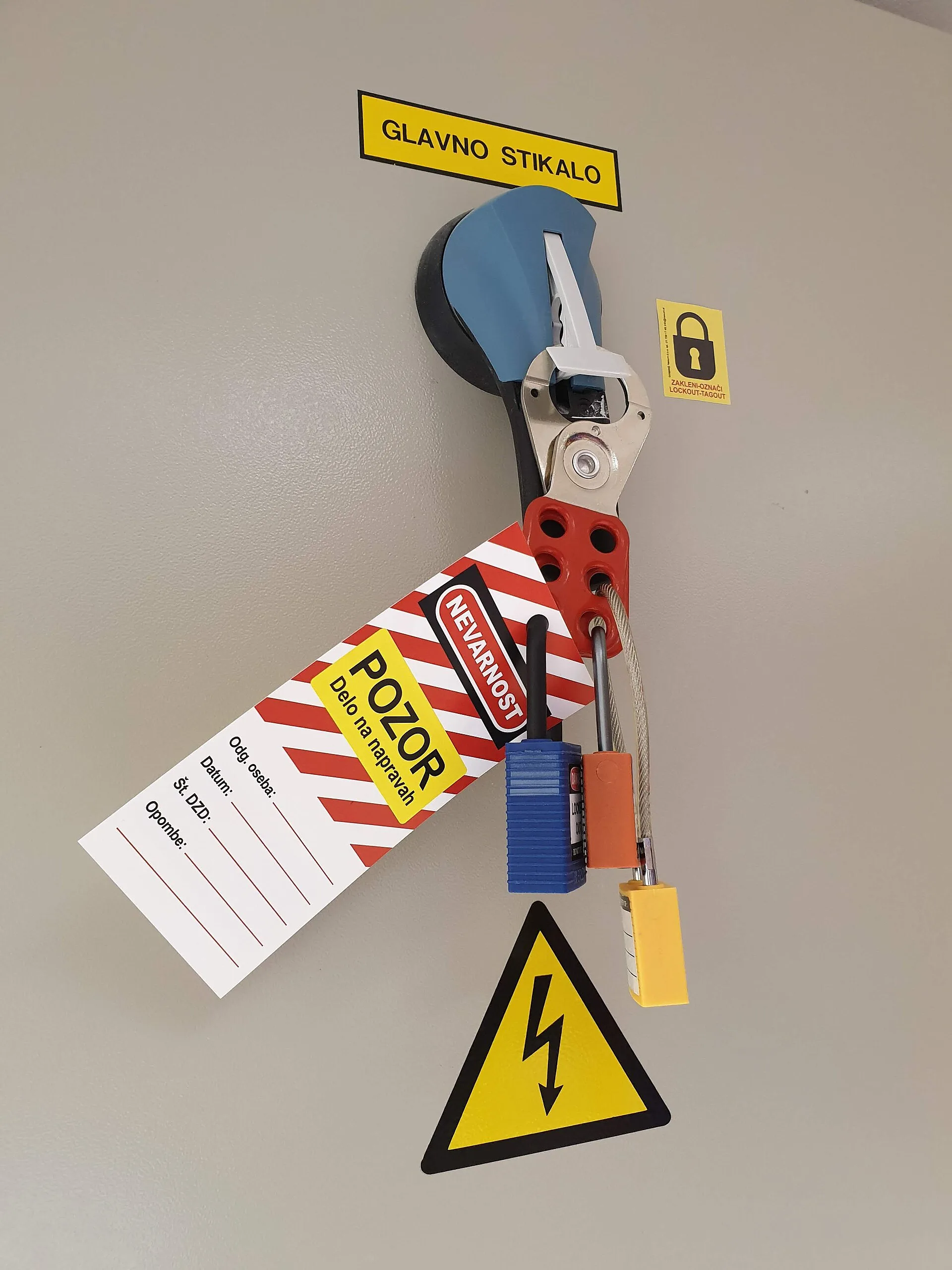 Electrical main switch locked out with a red lockout hasp, multiple coloured safety padlocks and a danger tag