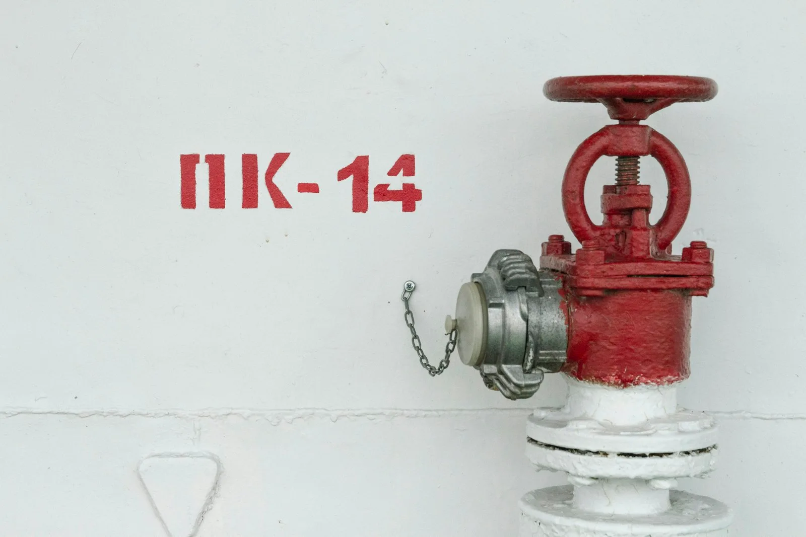Red internal fire hydrant landing valve with capped outlet on a white wall