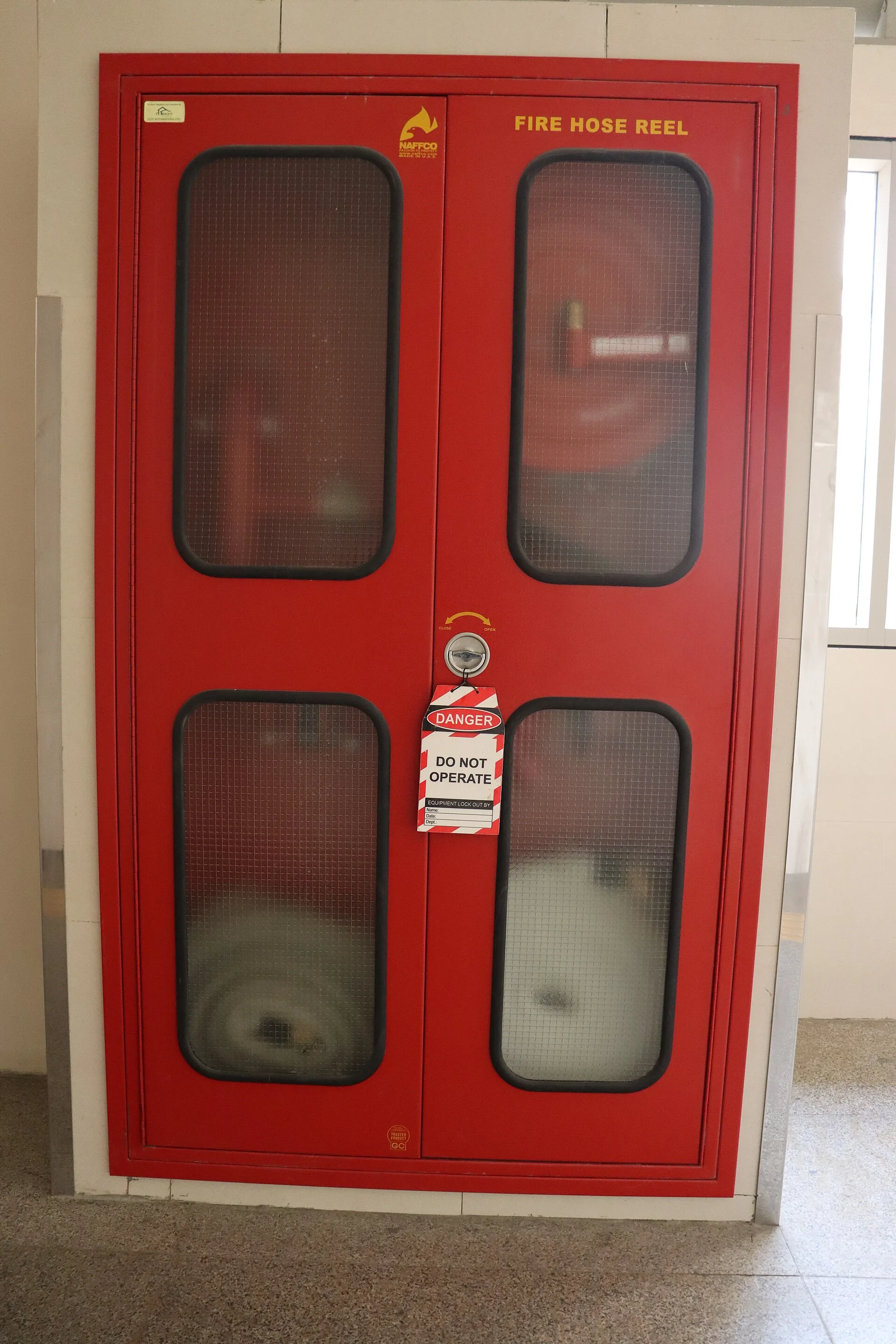 Red double-door fire hose reel cabinet with glazed panels and a do-not-operate tag
