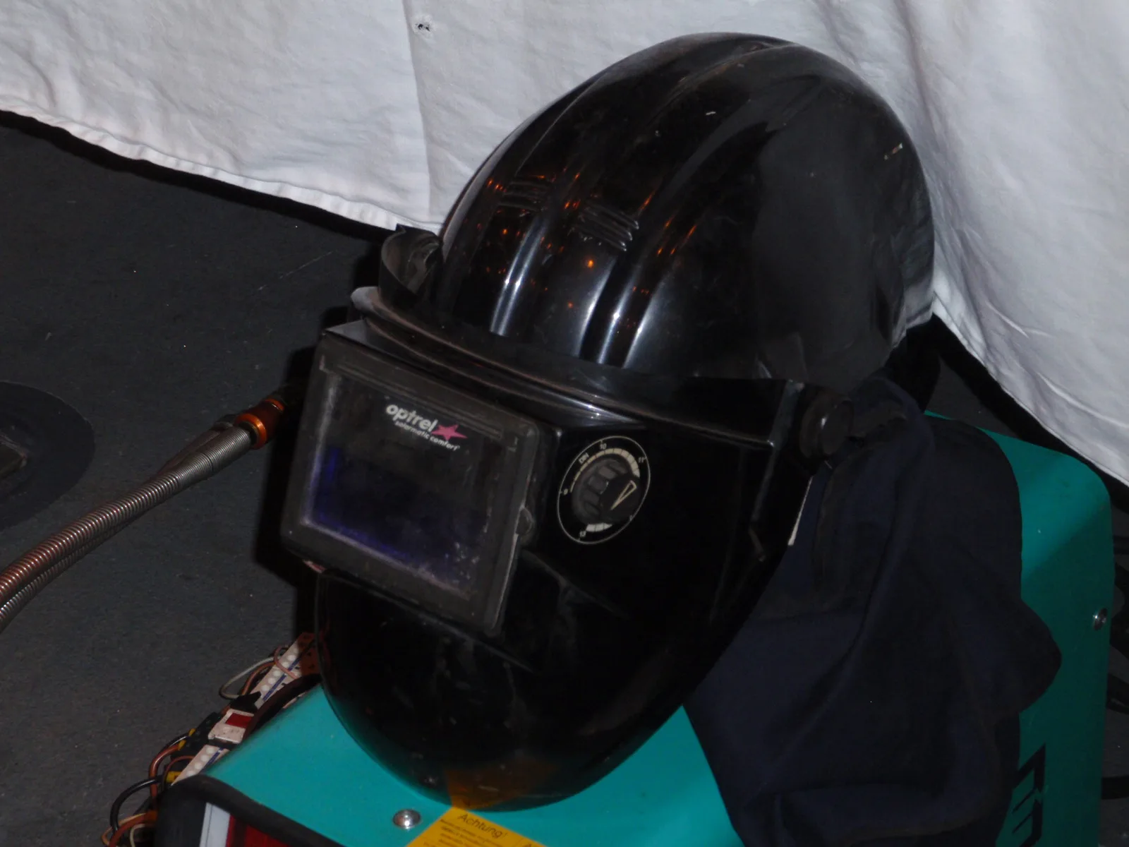 Black auto-darkening welding helmet resting on a welding machine