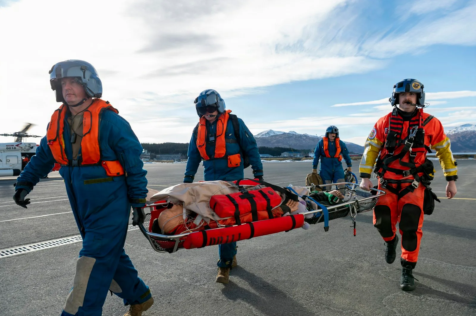 Rescue crew carrying a casualty secured in a red basket stretcher across an airfield