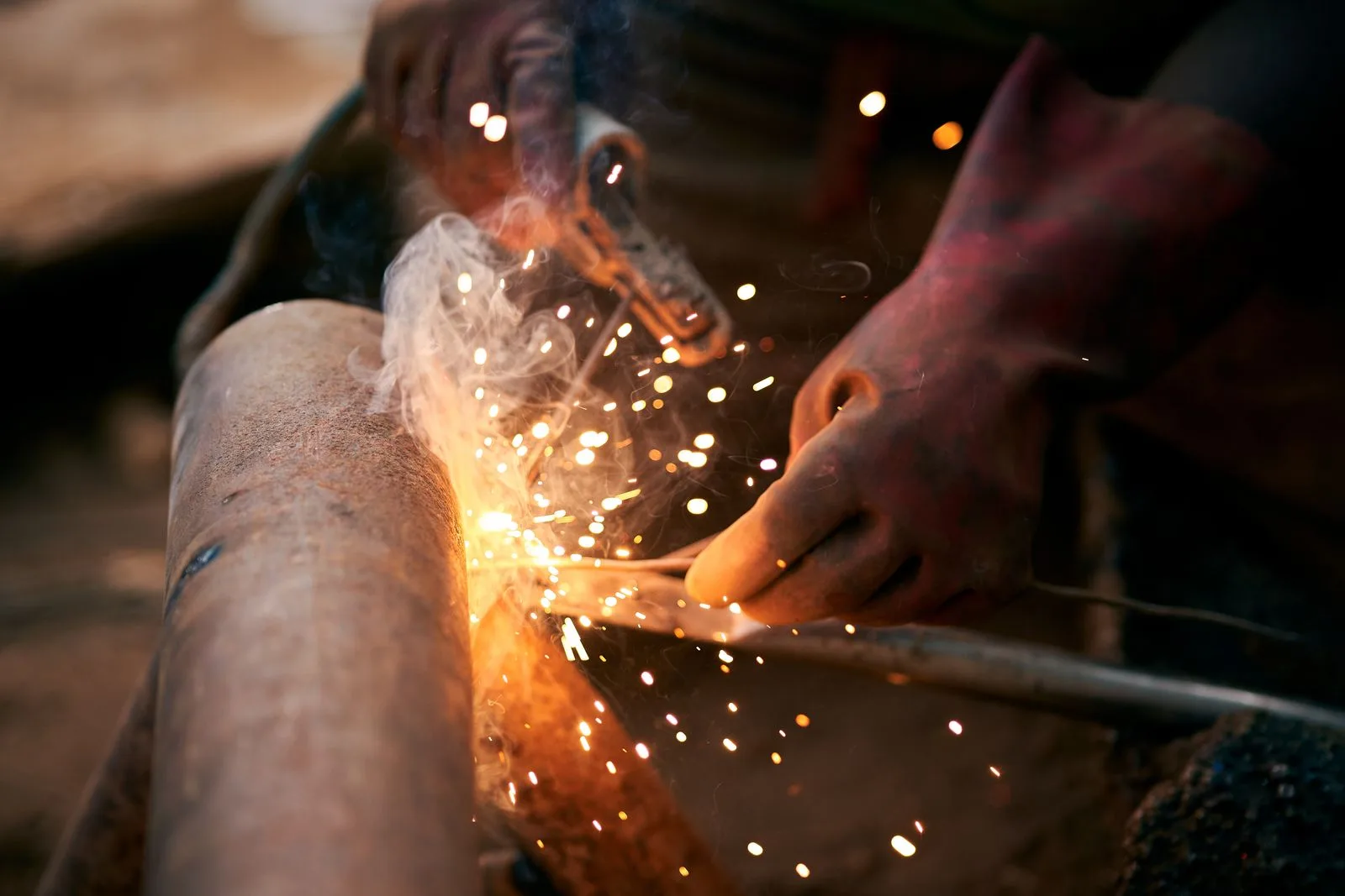 Welder's gloved hands working on a steel pipe amid flying sparks