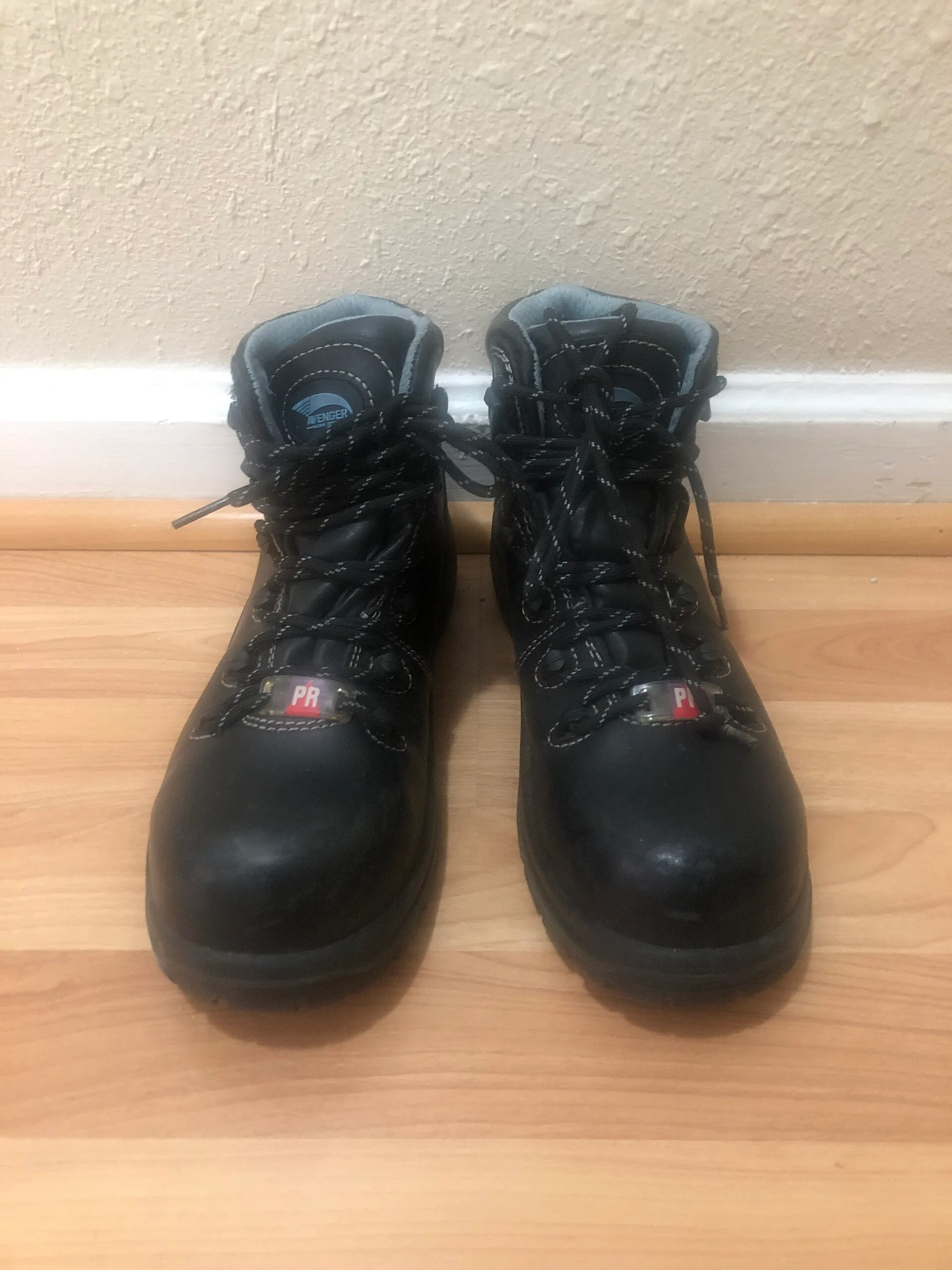 Pair of black steel toe work boots on a wooden floor