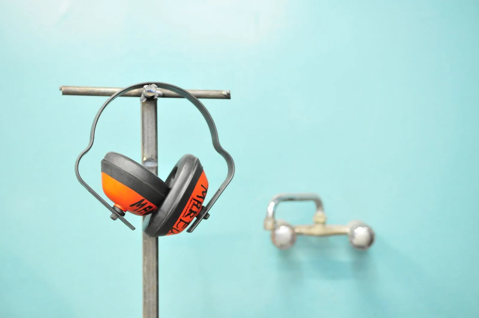 Orange and grey earmuffs hanging on a metal stand against a teal wall
