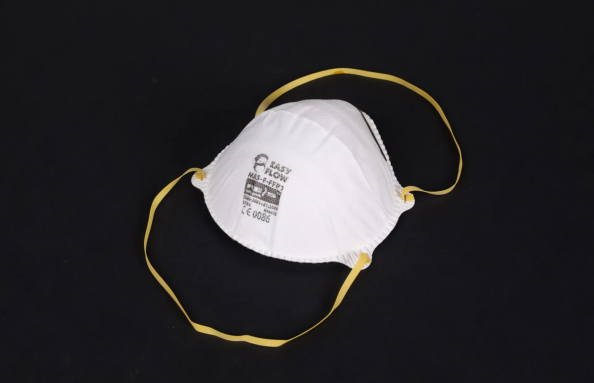 White moulded cup-style disposable FFP respirator with yellow elastic straps on a black background