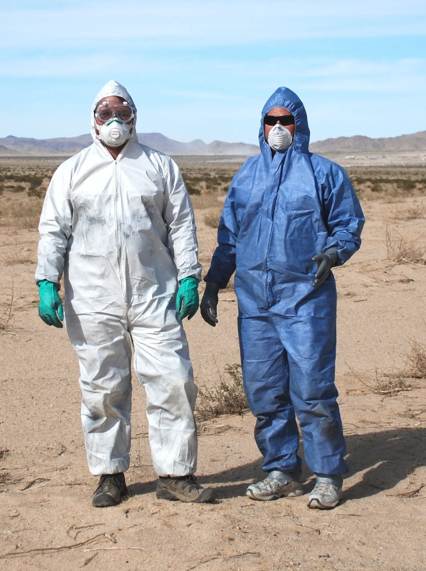 Two workers in white and blue hooded disposable coveralls with gloves and respirators