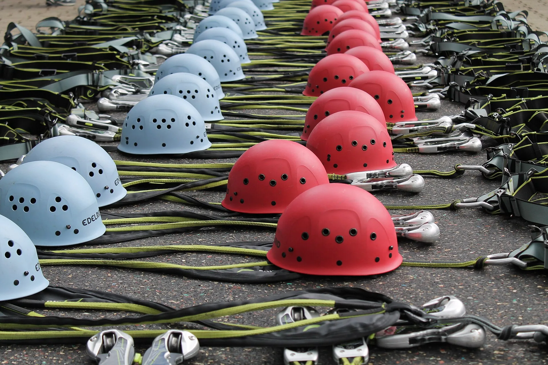 Rows of light-blue and red vented climbing helmets laid out with harnesses and lanyards