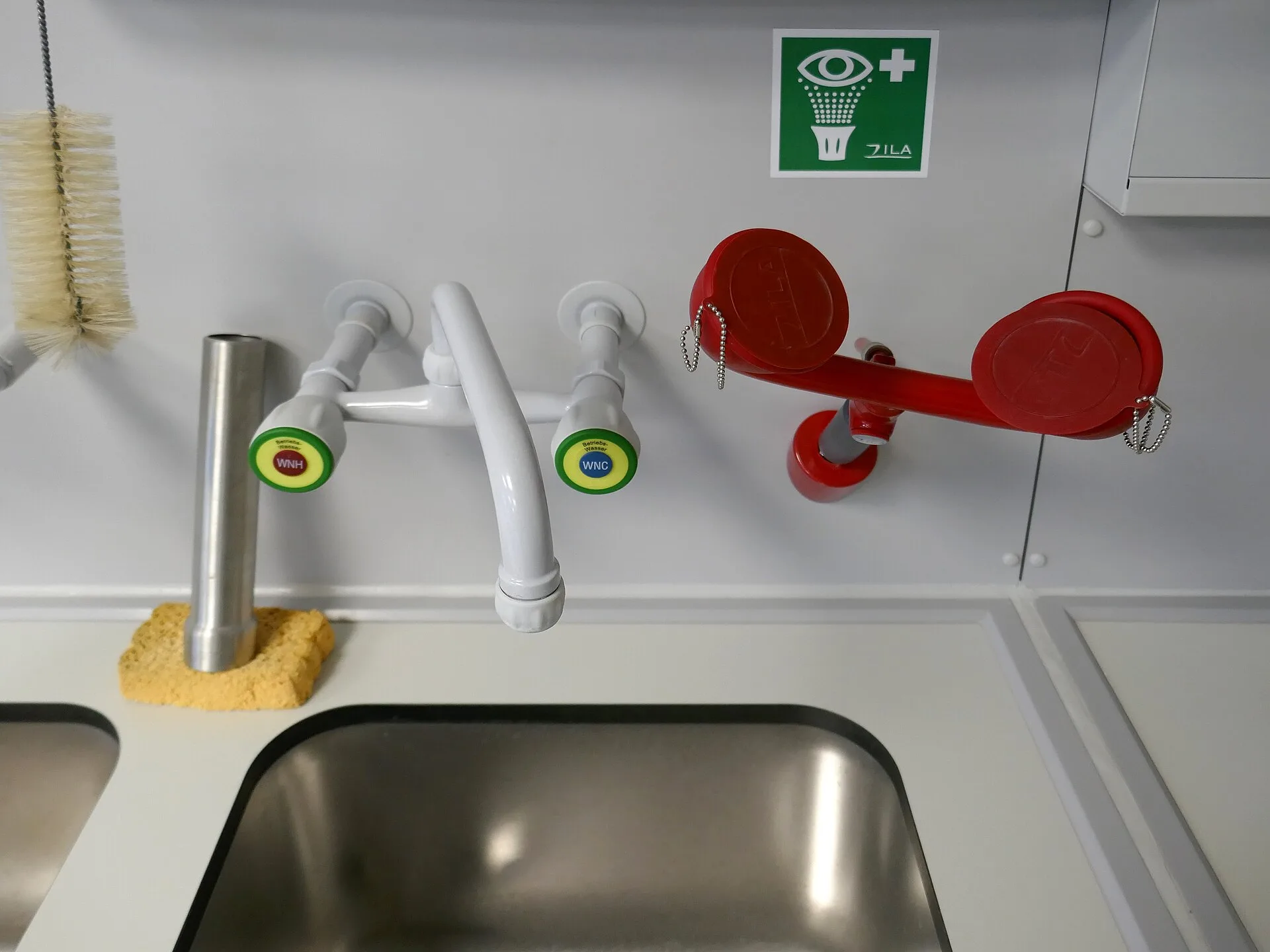 Laboratory sink with deck-mounted eyewash outlets and red swing-down eyewash below an eyewash sign