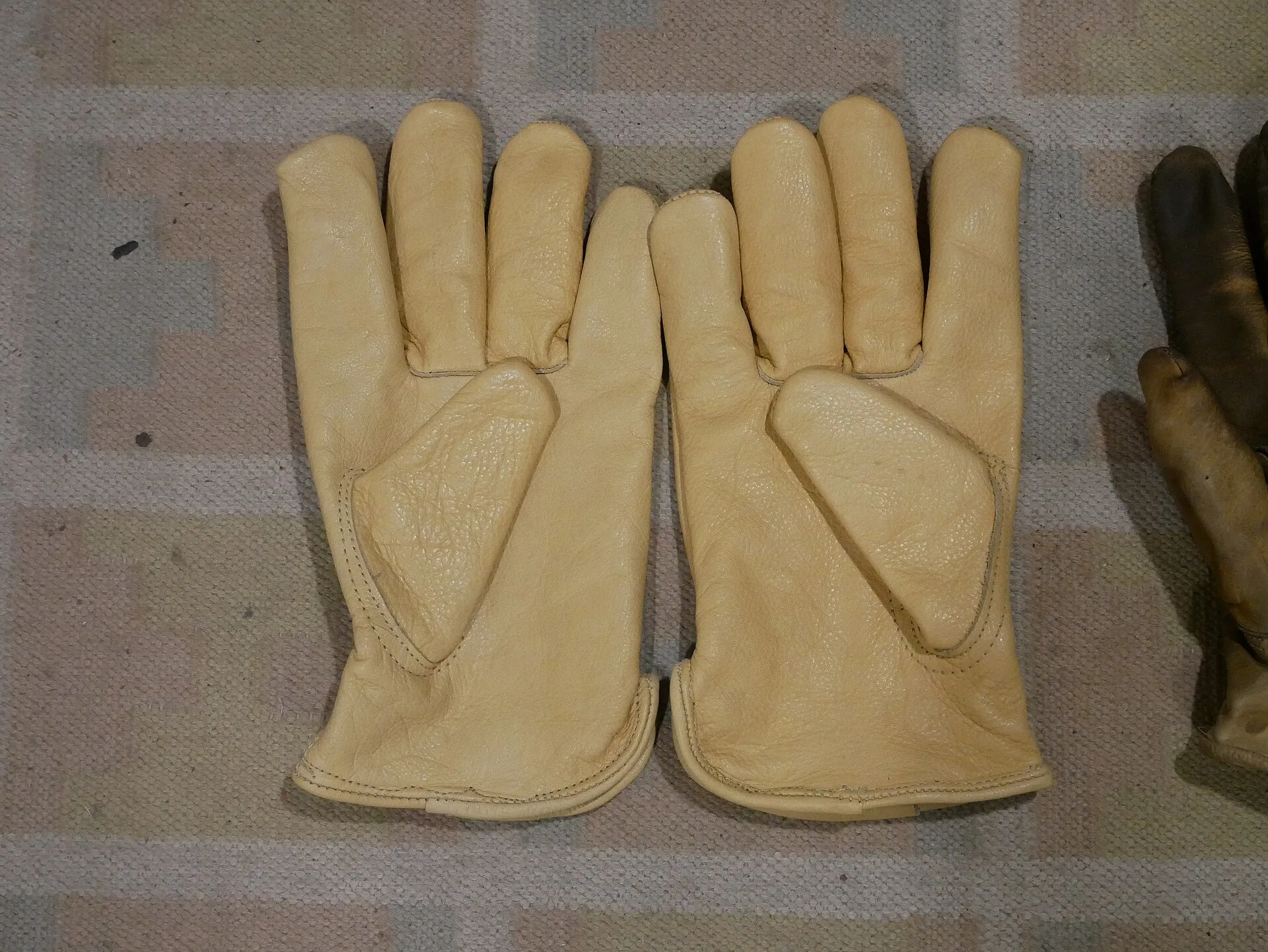 Pair of new tan cowhide leather work gloves laid flat