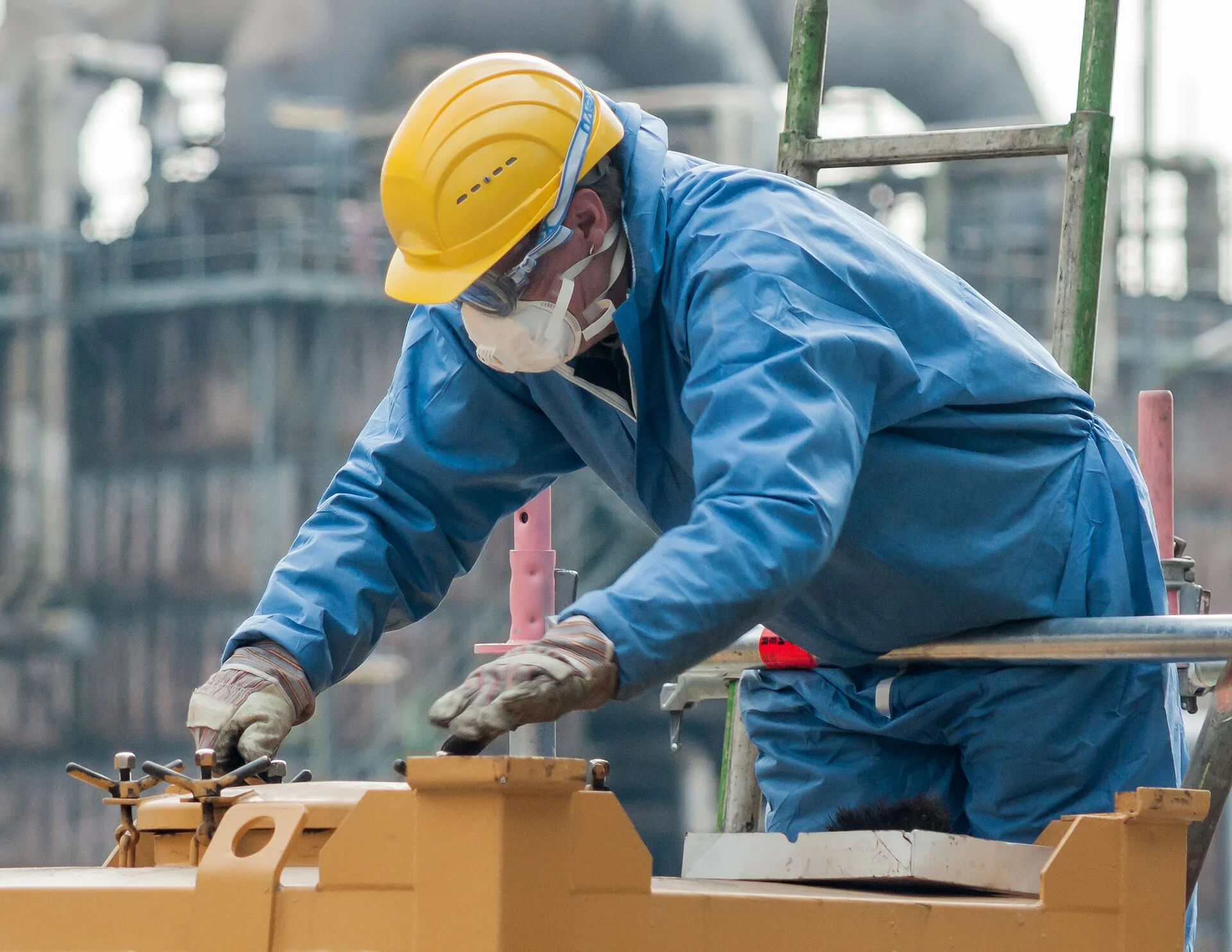 Industrial worker in blue coverall, hard hat, dust mask and gloves at a plant