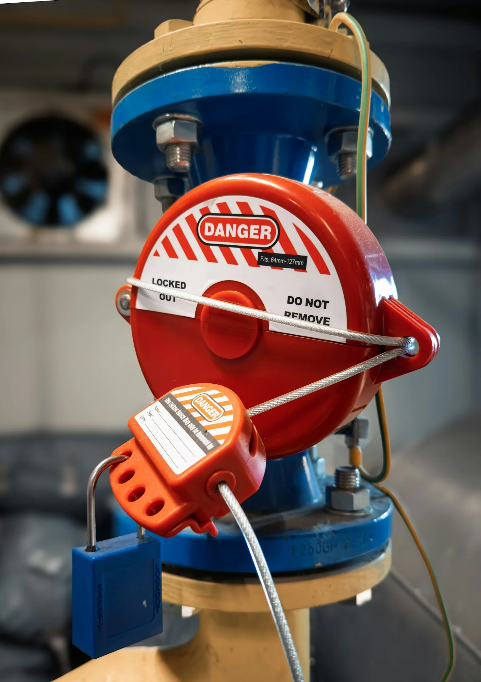 Red gate-valve lockout device with DANGER do-not-remove label, cable lock and blue safety padlock on a pipe valve