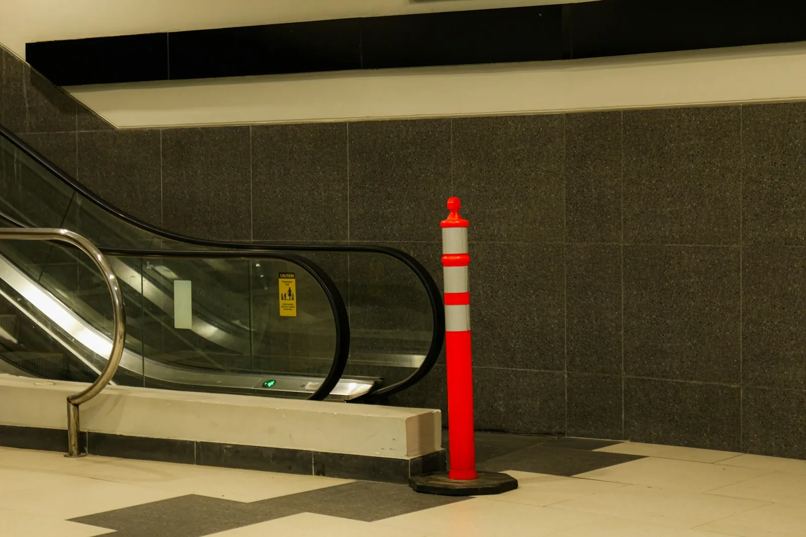 Orange delineator post with reflective bands on a weighted base beside an escalator
