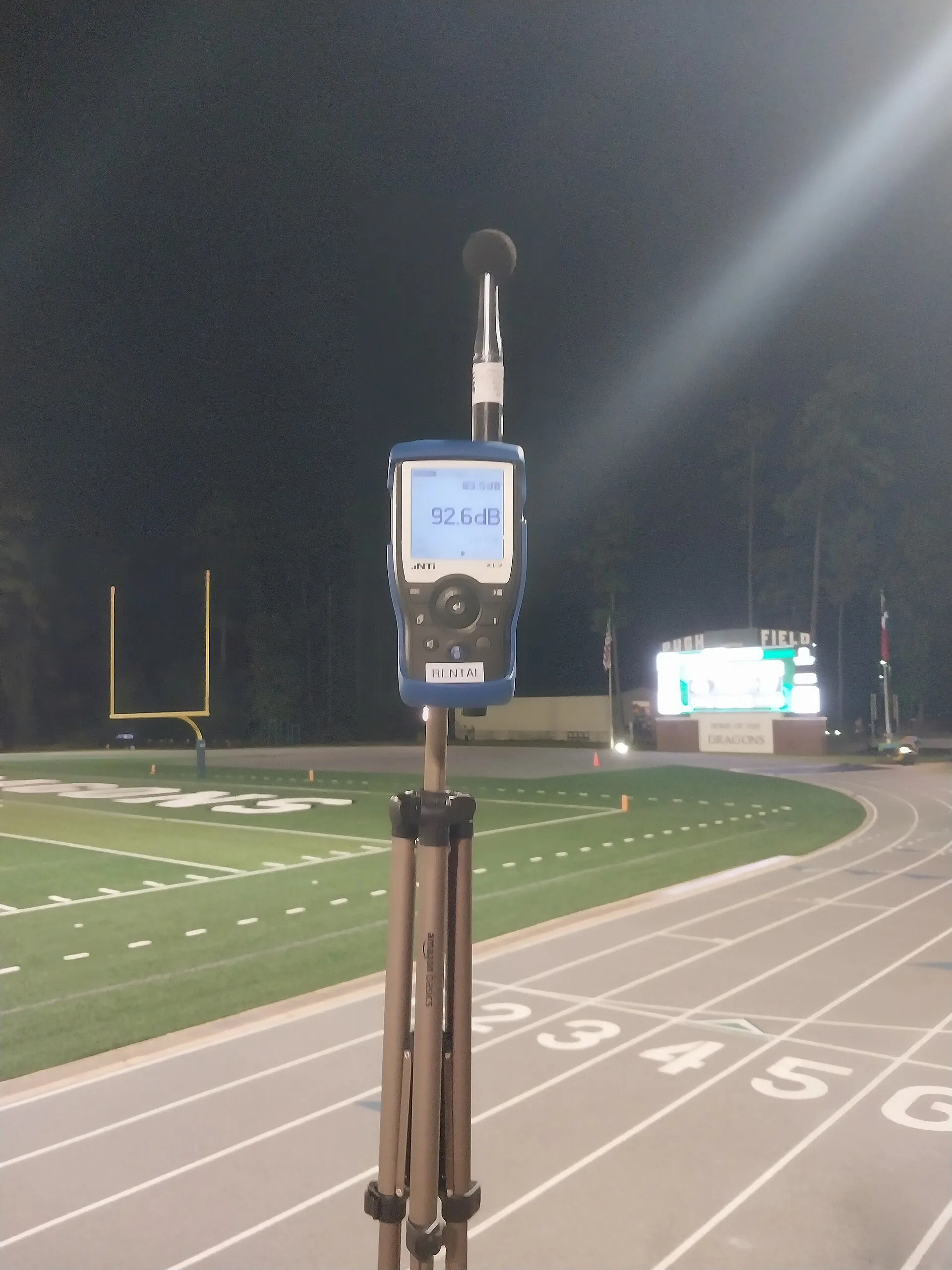 Sound level meter with foam windscreen mounted on a tripod for noise monitoring at a stadium