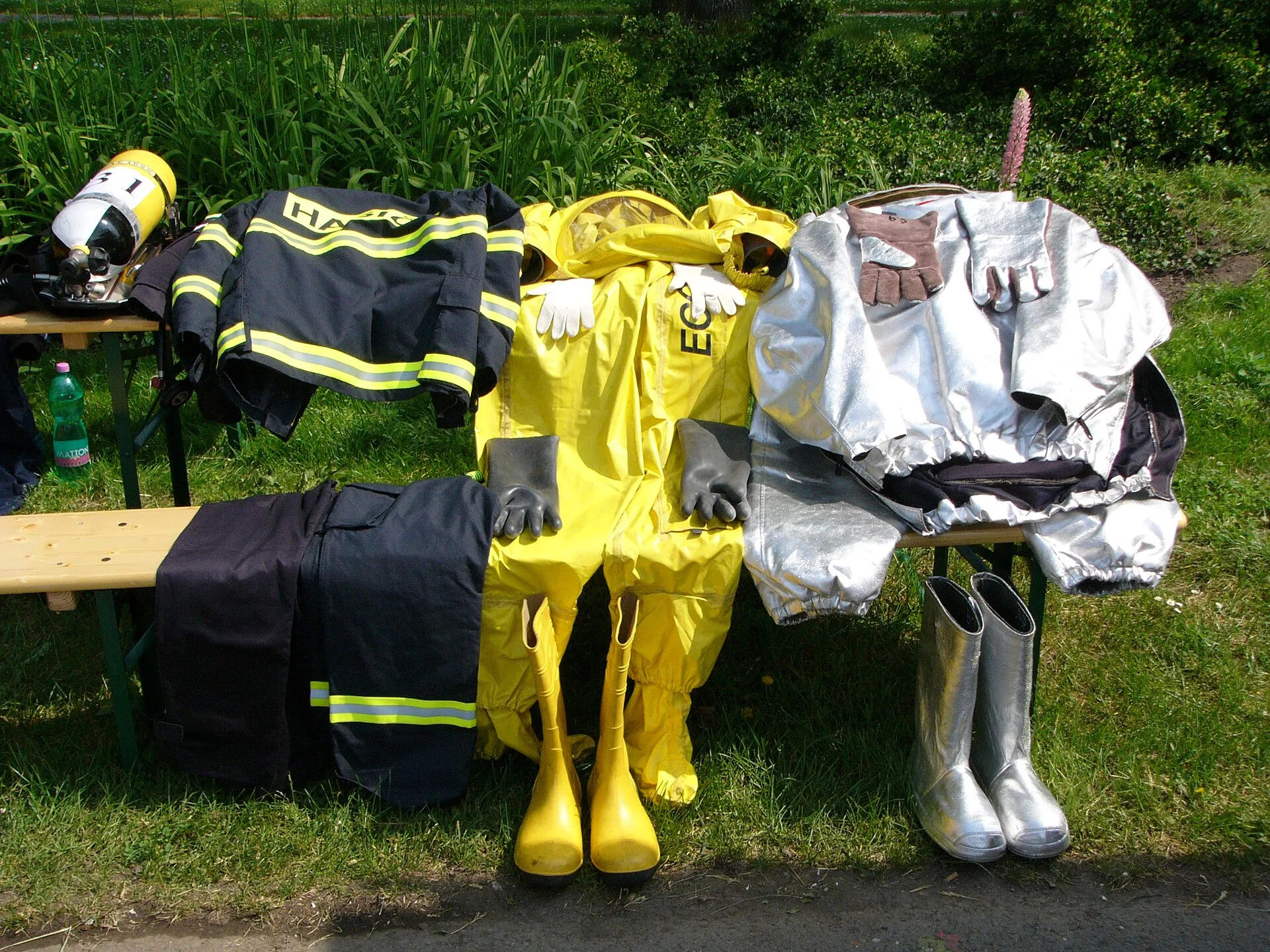 Firefighter turnout gear, yellow chemical protective suit and aluminised proximity suit with boots laid out on a bench