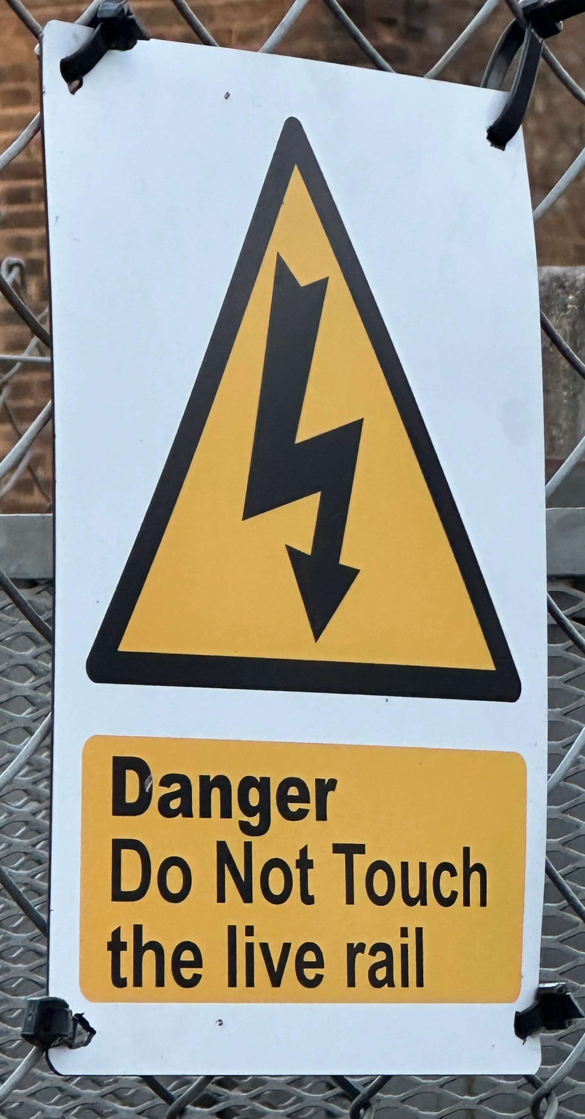 Yellow electrical hazard warning triangle with Danger Do Not Touch sign on a fence
